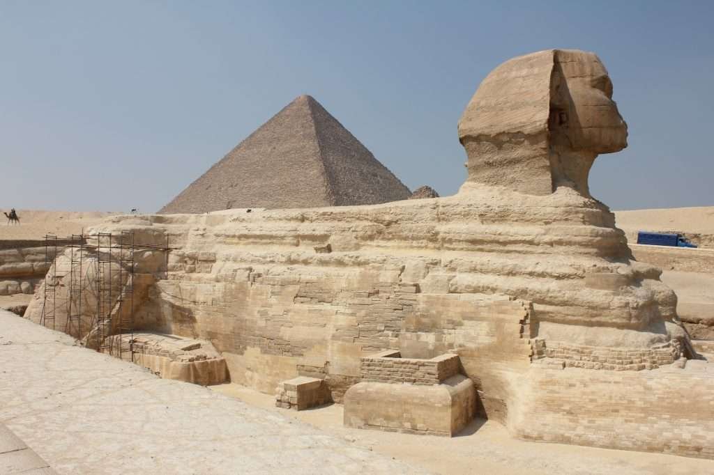 Picture of a historic sphinx in the middle of a typical Egyptian scenery under the clear sky and with pyramid in the background. Picture of a historic sphinx in the middle of a typical Egyptian scenery under the clear sky and with pyramid in the background.