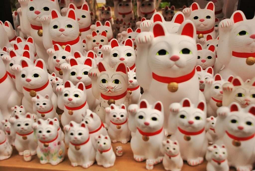 Maneki-neko (beckoning cat) - white cat figurine with raised arm on left side and red collar around neck.
