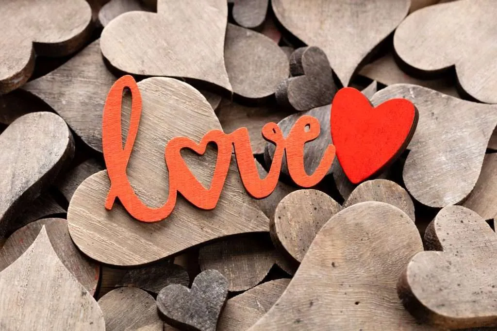 Wooden hearts, one red heart on the heart background with red letters that say love. The o in the word love is a heart.