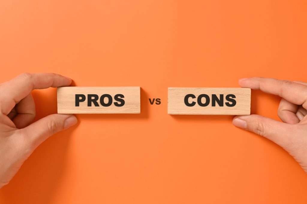 Two hands holding pros and cons text on wooden blocks which is saying pros vs cons with an orange background.